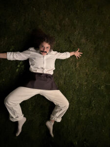 Person lying on grass in white clothing and a mustache
